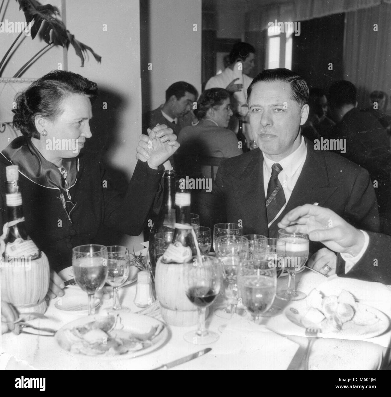 Wedding relatives happy eating giving challenge hands during a 1960s 1970s wedding in Italy. Black and white square shot. Stock Photo