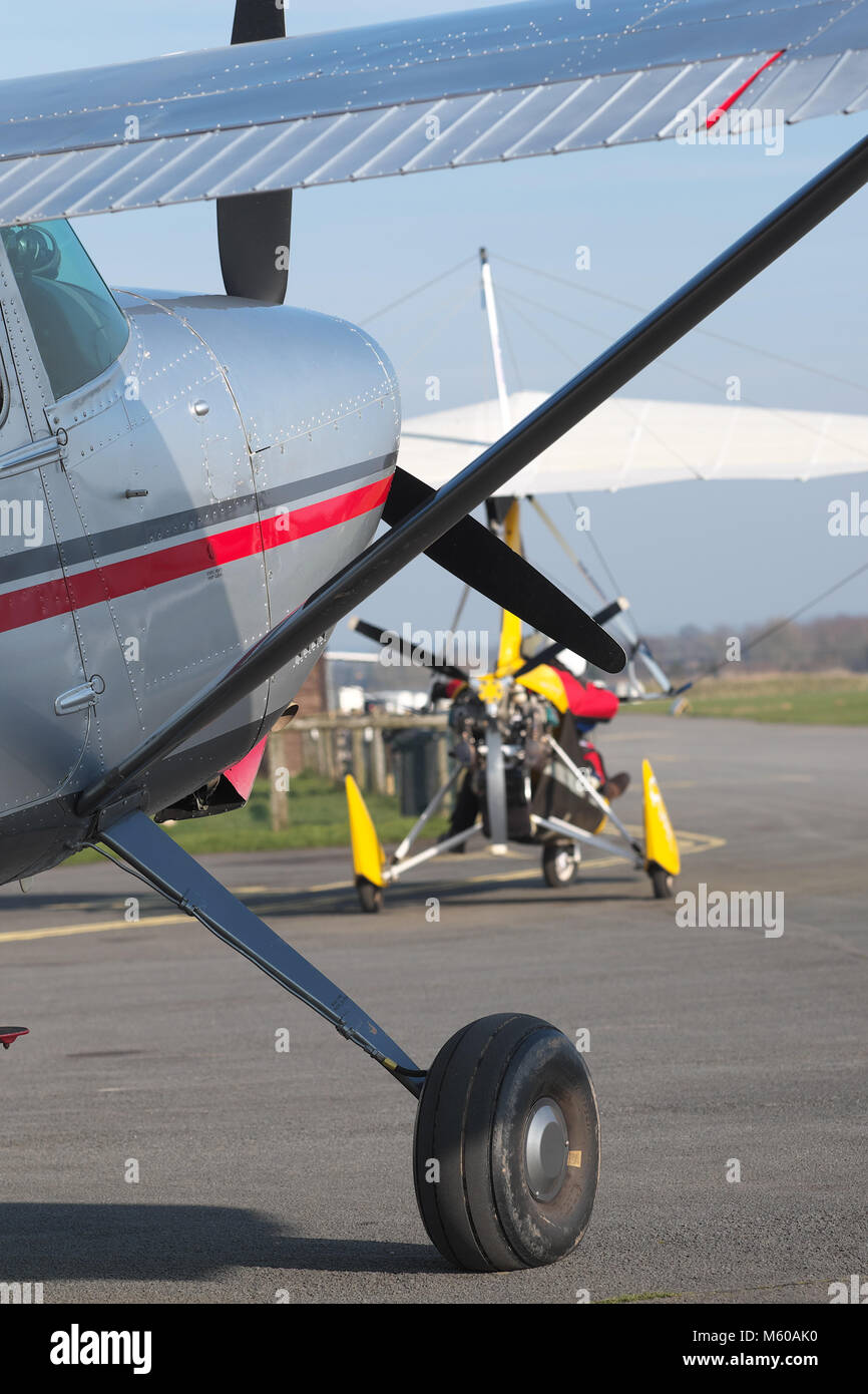 General aviation Cessna 185 light aircraft with a yellow flex wing microlight behind on airfield apron Stock Photo