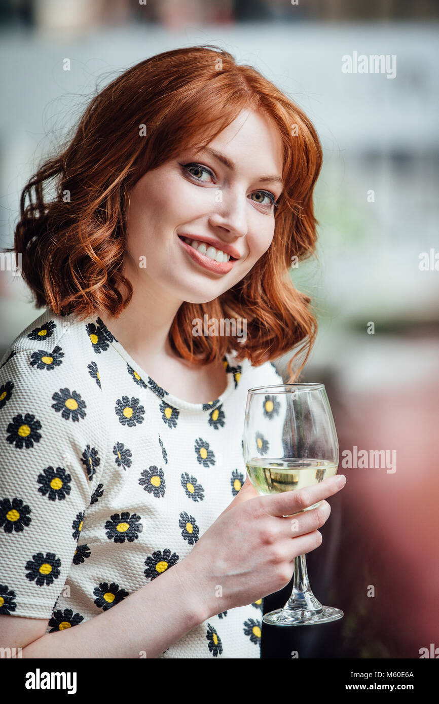 Portrait of a beautiful, redheaded woman with a glass of wine at a social event. Stock Photo