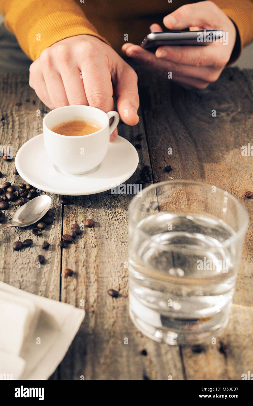 Man drink coffee while using a smartphone, glass of water and newspaper on table. Stock Photo