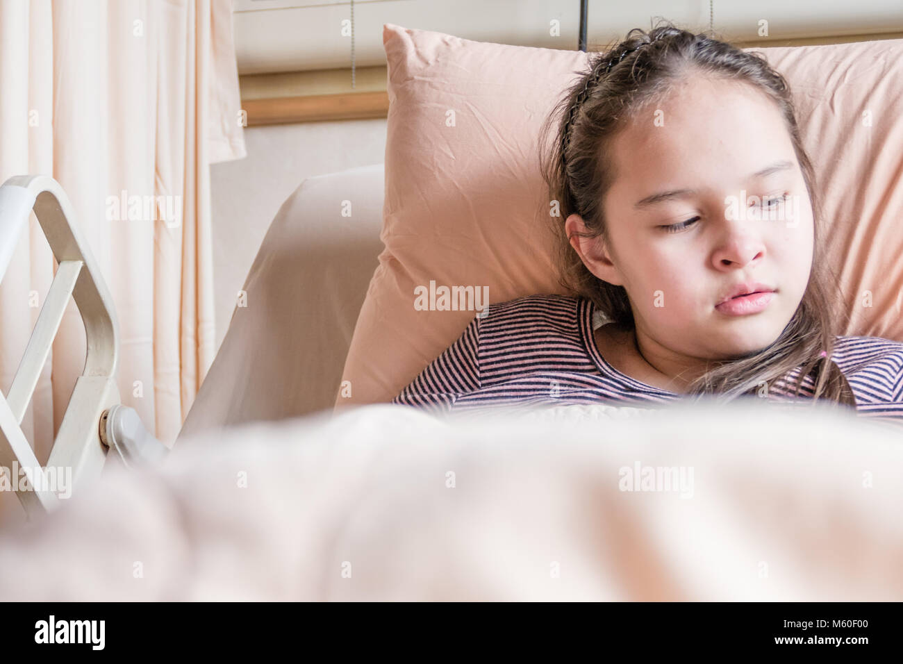 Asian American tween girl lying in hospital bed, health care concept Stock Photo