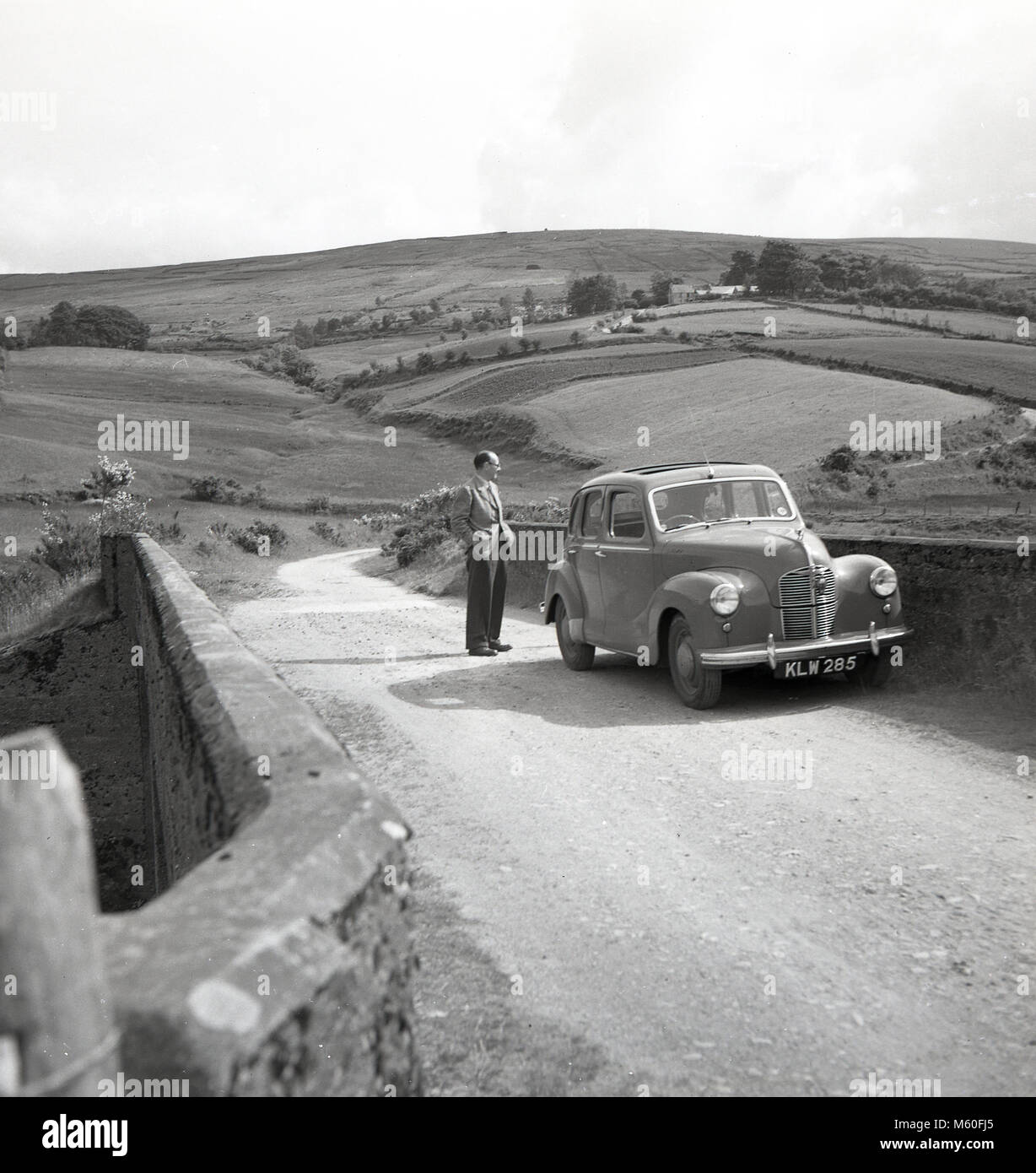 1950s, historical, Ireland, rolling hills, on a quiet country lane a driver outside his car at a bridge looks at the view. Stock Photo
