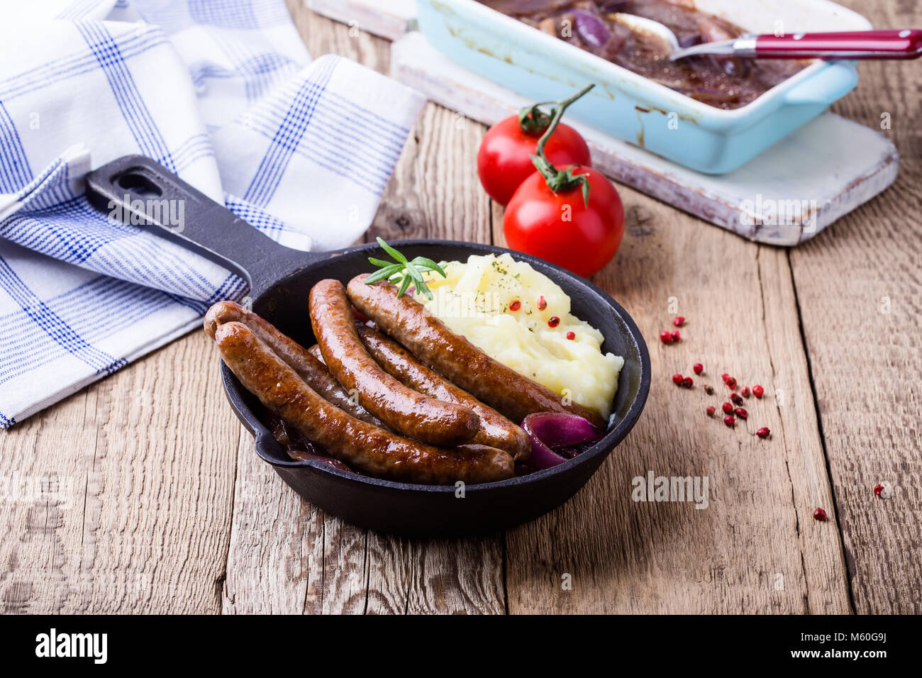 Sausage and onion casserole served with potato mash in cast iron skillet on rustic wooden table