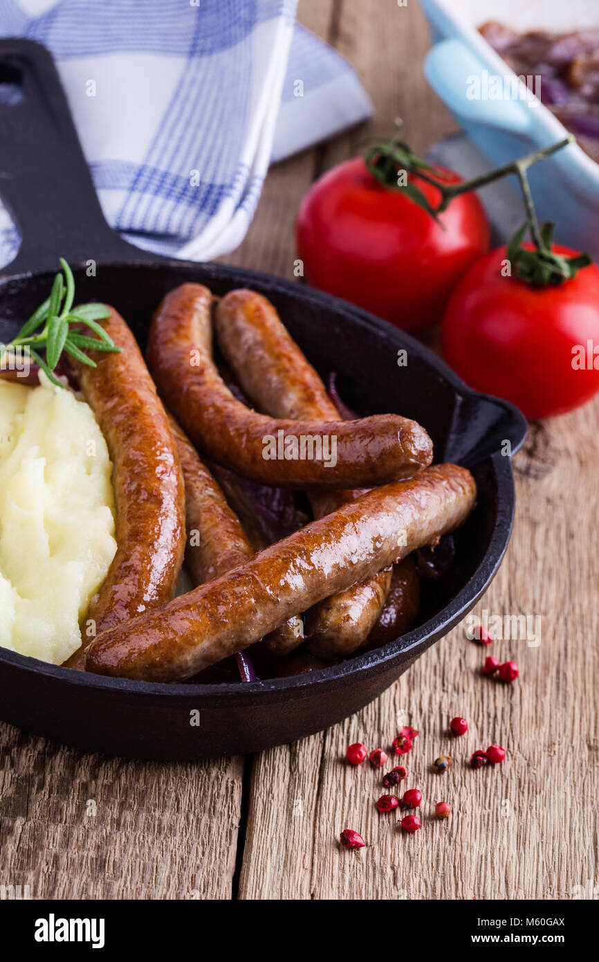 Sausage and onion casserole served with potato mash in cast iron skillet on rustic wooden table Stock Photo