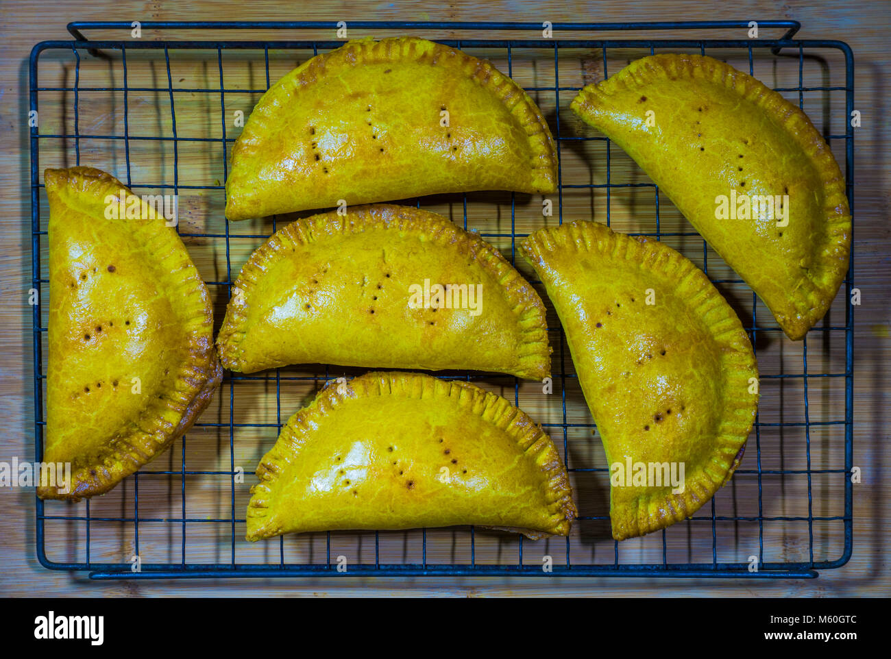 Savoury baked Jamaican patties - authentic Caribbean cuisine - fresh from the oven, and cooling down on mesh, ready to eat. Stock Photo