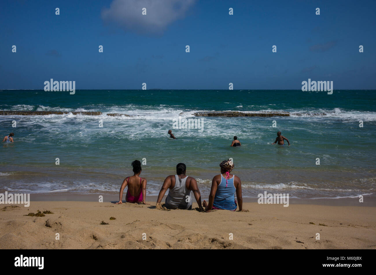 Foreign and local residents swim behind a natural breakwater in Bathway Beach located in the Levera National Park, Grenada. Situated on the windward side of Grenada, the seas are often too rough for swimming or sailing. Stock Photo