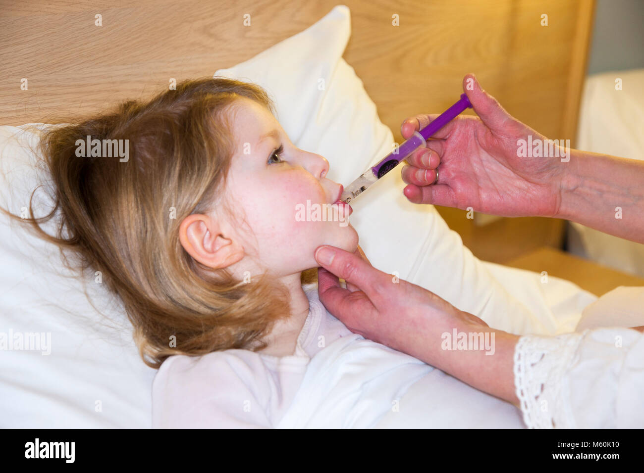 Mother / mum / mom giving Calpol medicine with paracetamol to – an apparently – sick / ill child / kid / girl in bed with fever or temperature. (95) Stock Photo