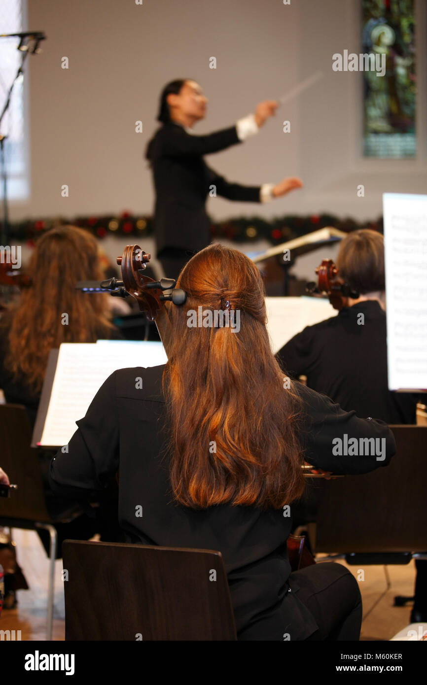 cellist playing in a concert, with a blurred female conductor on the rostrum. Stock Photo