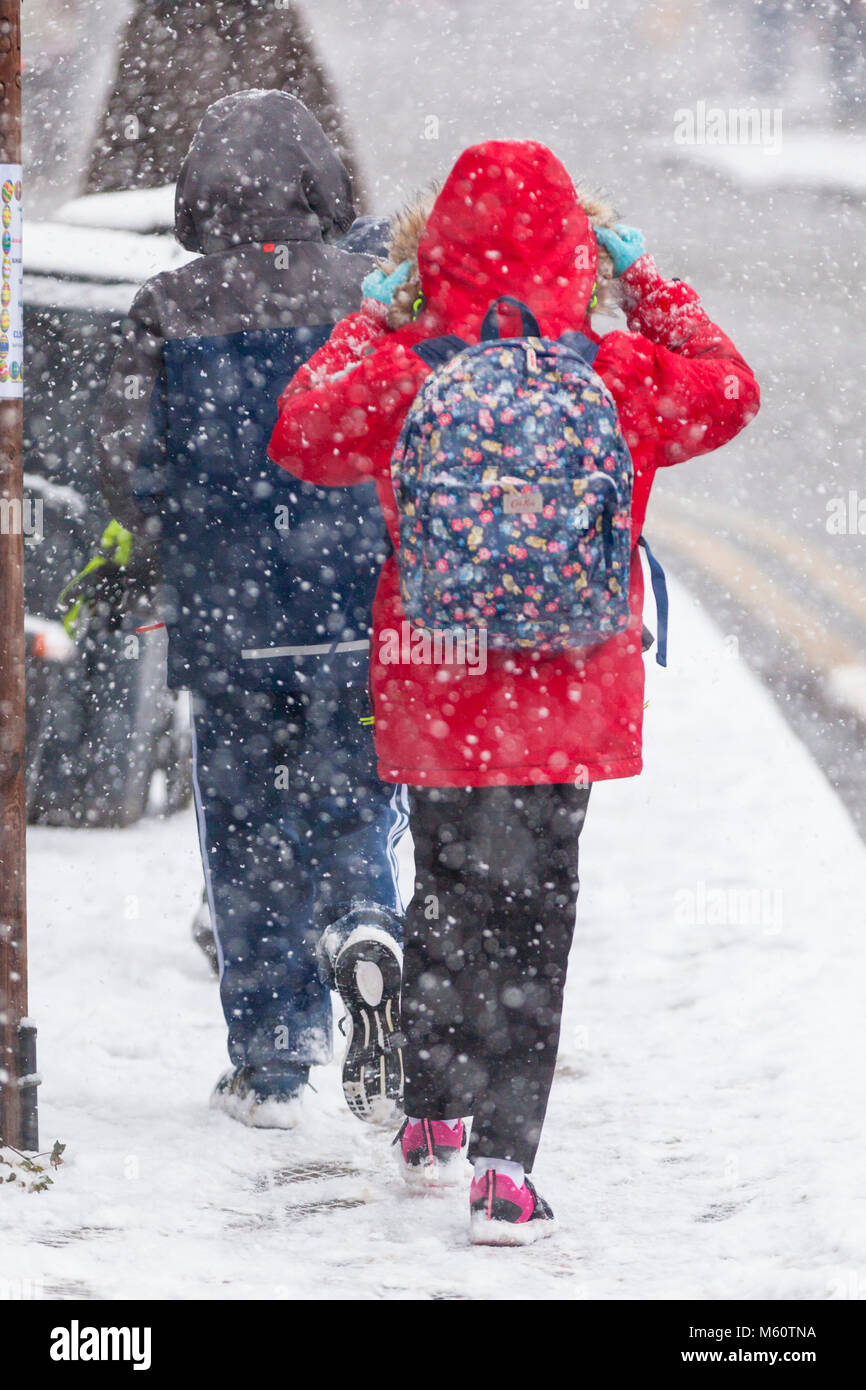 little girl with a bright red jacket and colourful school bag strapped on her back walks through a snow 'Beast from the East' kent uk Stock Photo