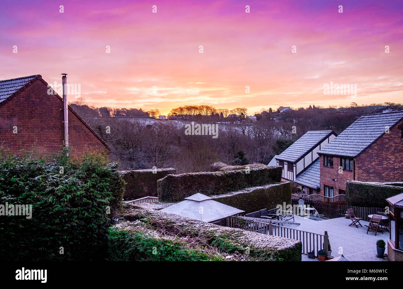 Swansea, Wales, UK. 27th Feb 2018. UK Weather: Suburbia back gardens covered in snow from The Beast in the East, with a vivid sunrise above the hills and trees Credit: Sian Pearce Gordon/Alamy Live News Stock Photo