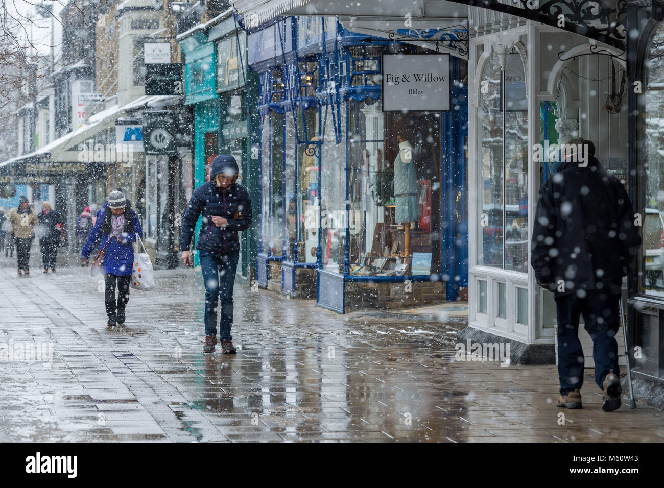 Ilkley, West Yorkshire. 27th Feb, 2018. UK Weather: People in Ilkley,  heads bowed, dressed in winter clothing with hoods up or wearing hats, brave the falling snow whilst walking past shops on The Grove. 27th February 2018, Ilkley, UK Credit: Ian Lamond/Alamy Live News Stock Photo