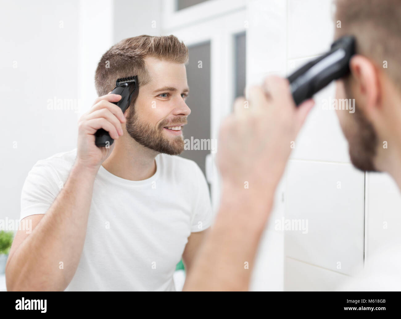 Handsome Bearded Man Cutting His Own Hair With A Clipper Stock