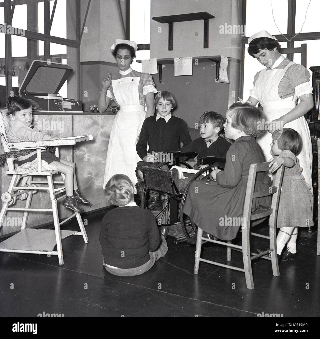 1950s, historical, female nurses looking after injured children in a hospital ward as they all sit listening to music from a portable record player, England, UK. Stock Photo