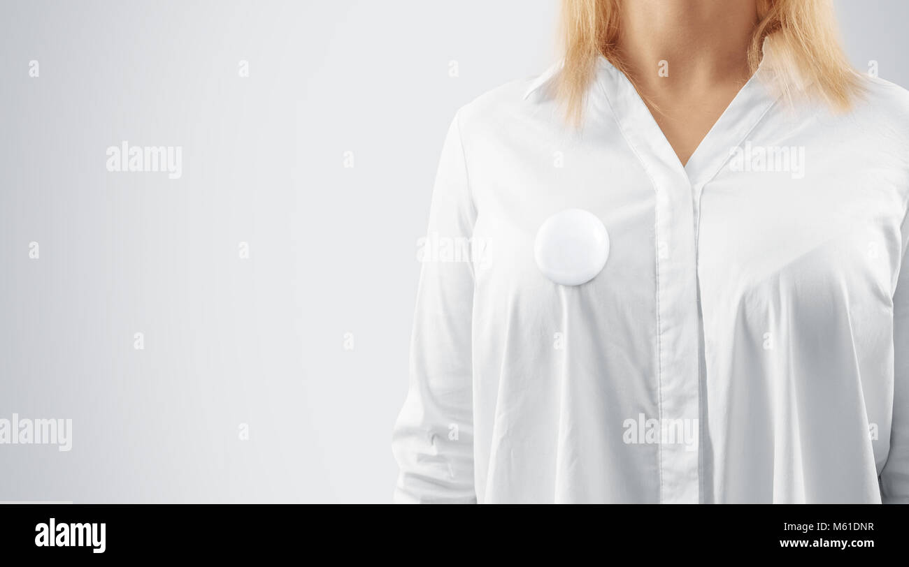 Blank button badge mockup pinned on the womans chest, close up view. Girl wear white shirt and campaign pin mock up. Volunteer round emblem design ele Stock Photo