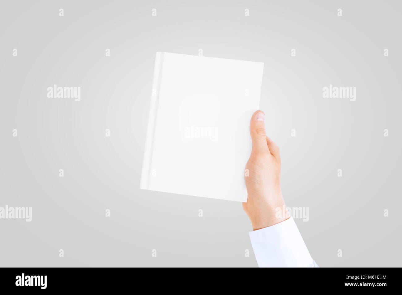Hand in white shirt sleeve holding closed blank book cover mock up in the hand. Book front holding in sleeve shirt hand. Vertical catalogue template m Stock Photo