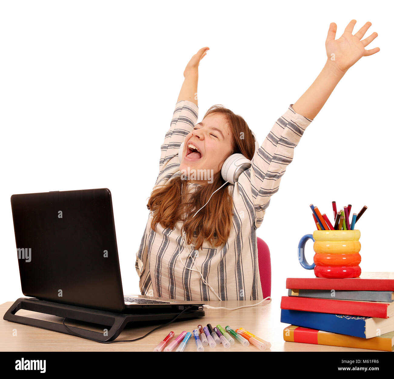 Happy little girl with hands up listens to music on laptop Stock Photo