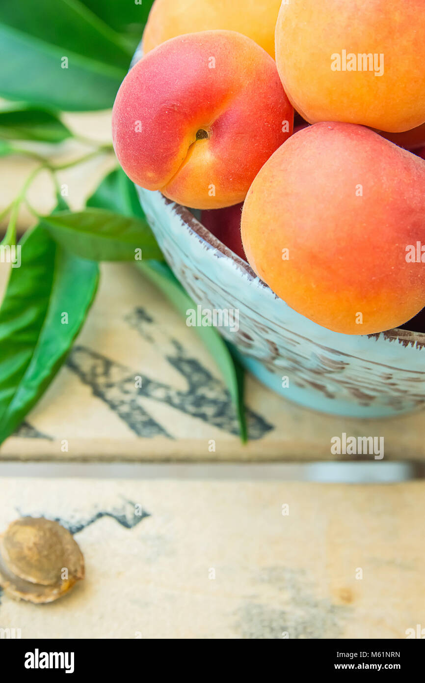 Bunch of Ripe Raw Fresh Colorful Apricots in Blue Ceramic Vintage Bowl on Wood Garden Table with Green Leaves and Kernel. Summer Vitamins Superfoods H Stock Photo