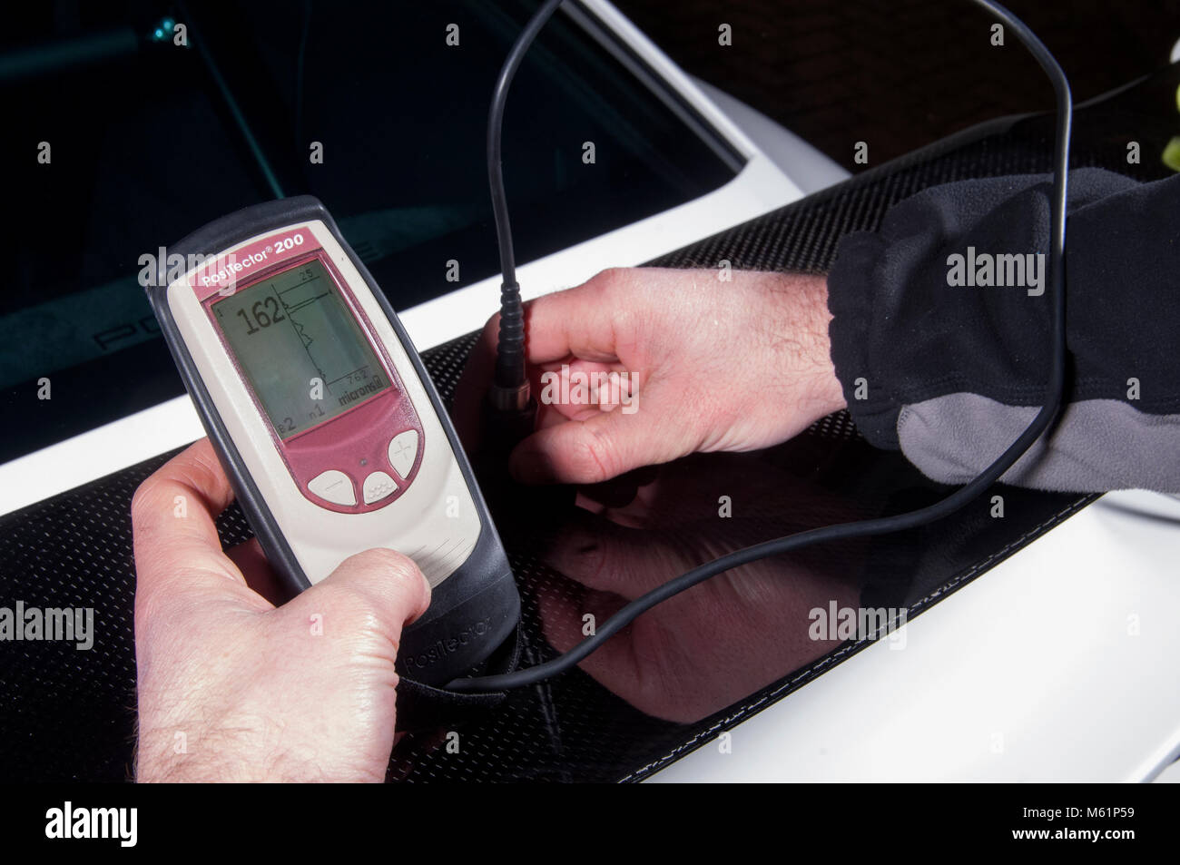 Car valeter measure paint depth while detailing a Porsche sports car