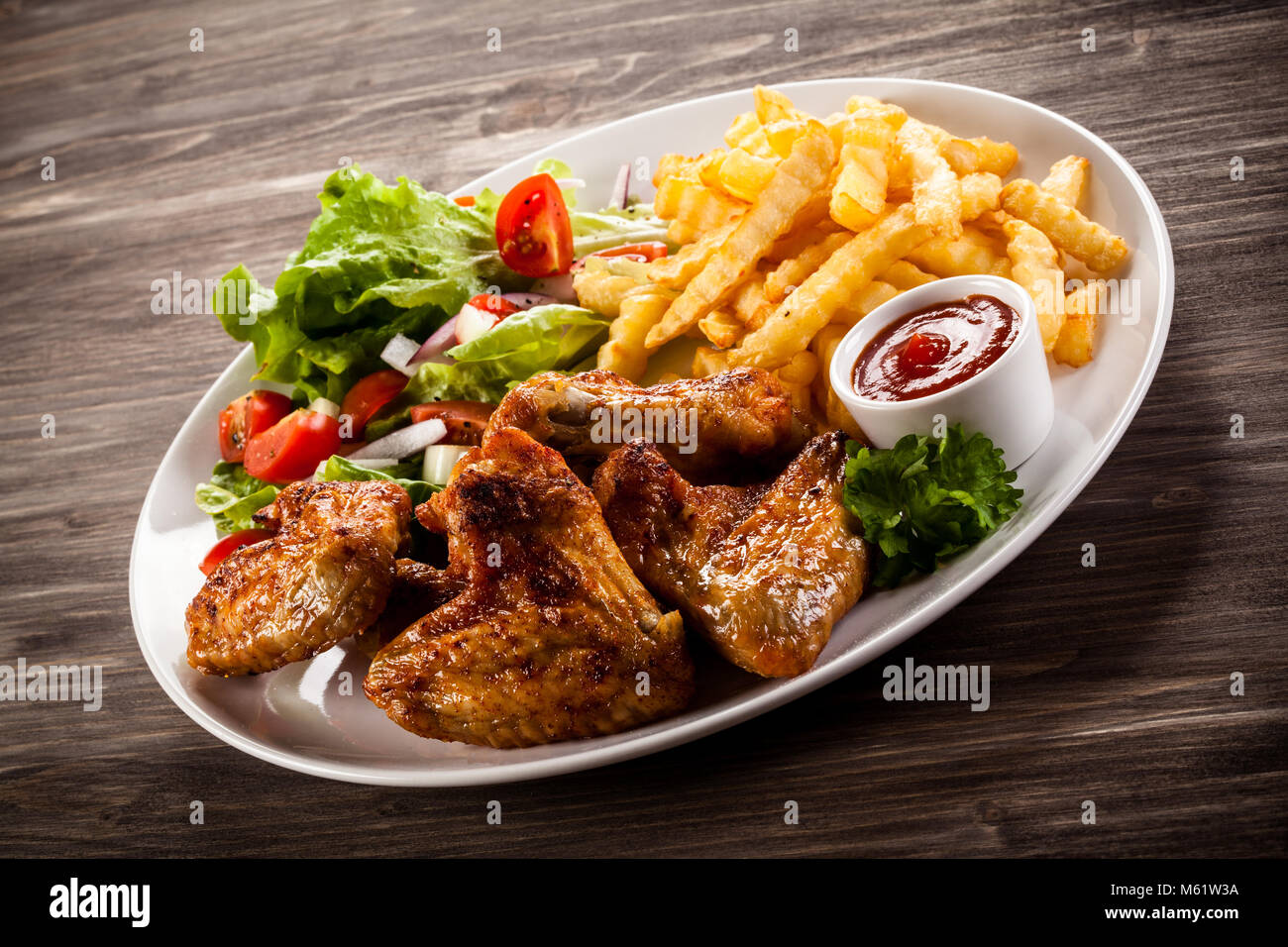 Grilled chicken wings, chips and vegetables on wooden table Stock Photo ...