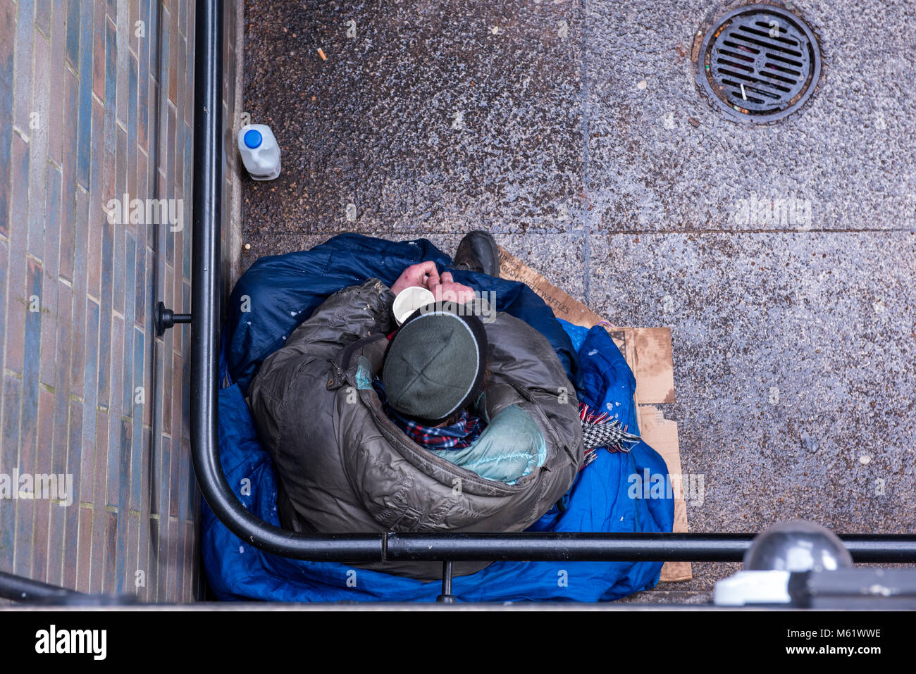 a homeless person sitting in a stairwell at the side of tower bridge in london. Vagrancy in the capital and cold sleeping rough on the streets outside Stock Photo