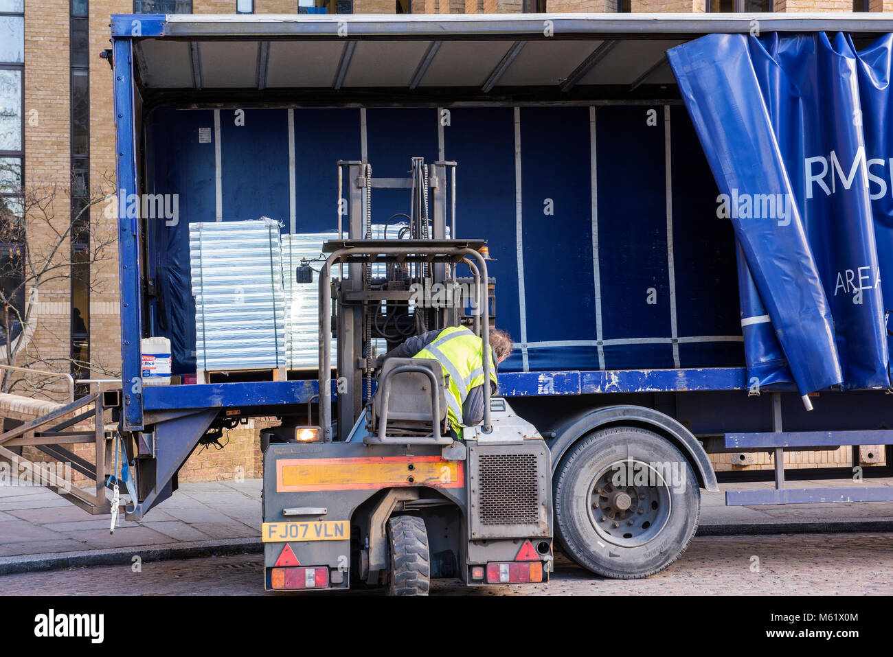 a man using a forklift truck to load or unload a curtain-sided lorry or truck trailer. Wagon being unloaded at a depot or warehouse by small forklift Stock Photo