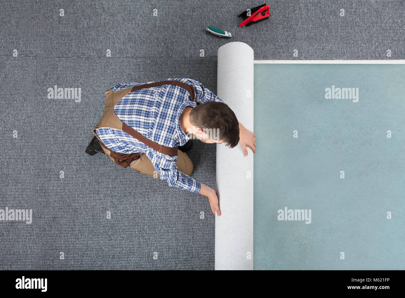 High Angle View Of Young Male Worker In Overalls Rolling Carpet On Floor At Home Stock Photo