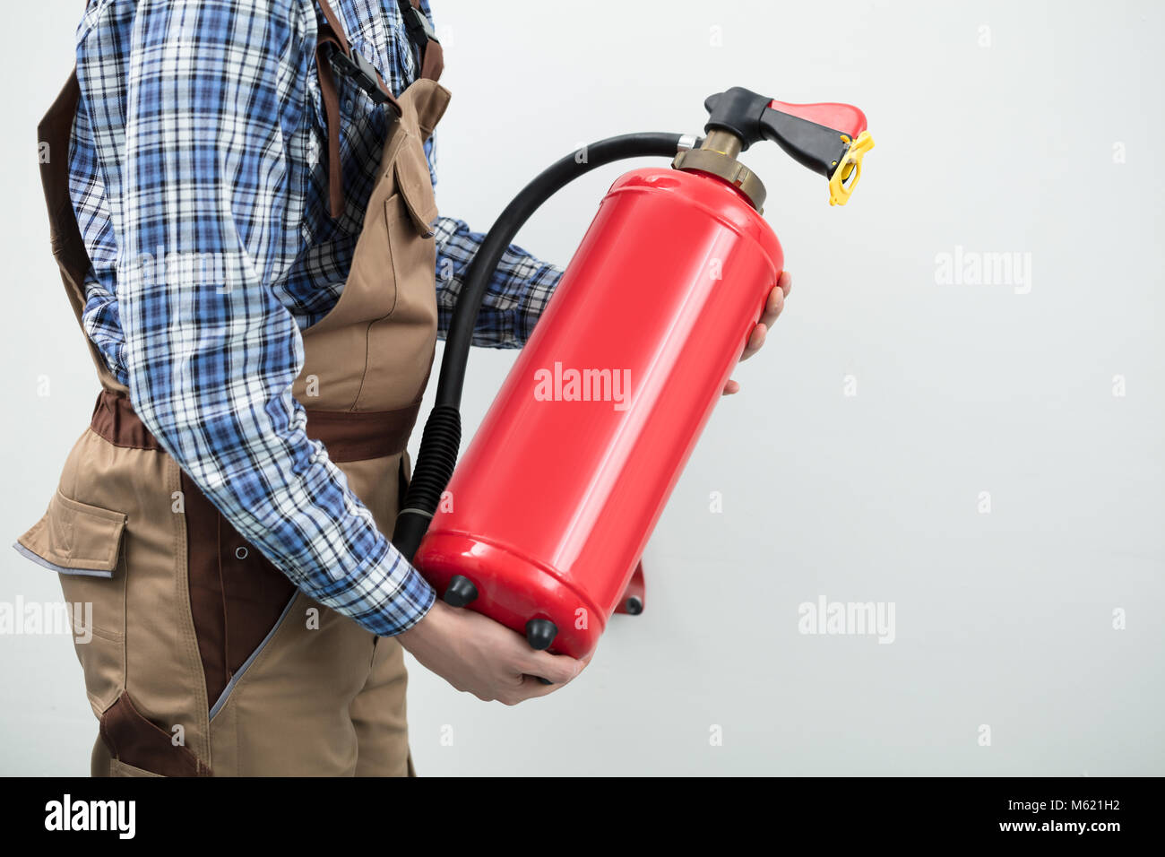 Young Technician Carrying Red Fire Extinguisher Against White