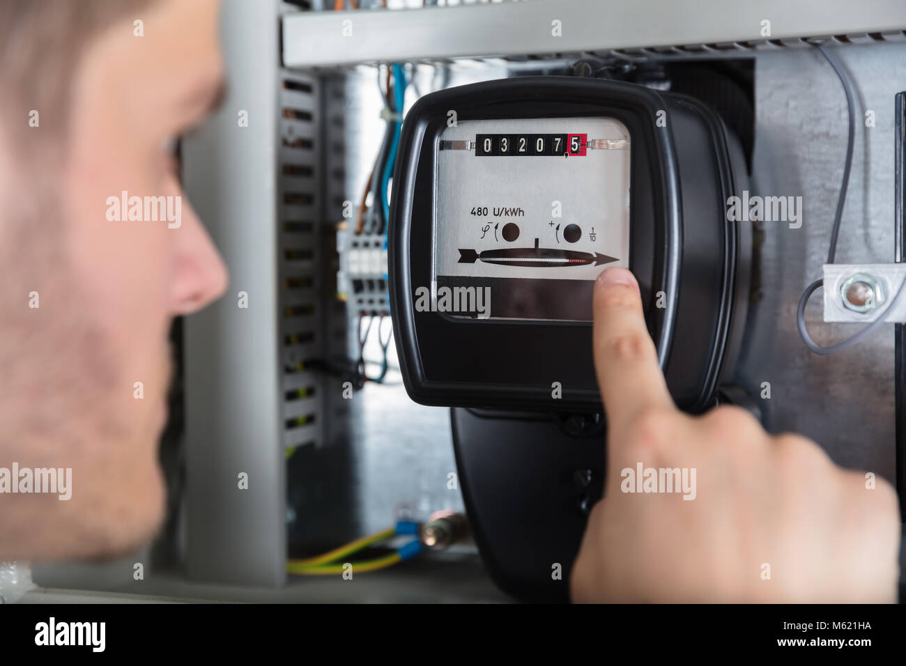 Close-up Of Young Man Pointing At Electric Meter In Fuse Box Stock Photo