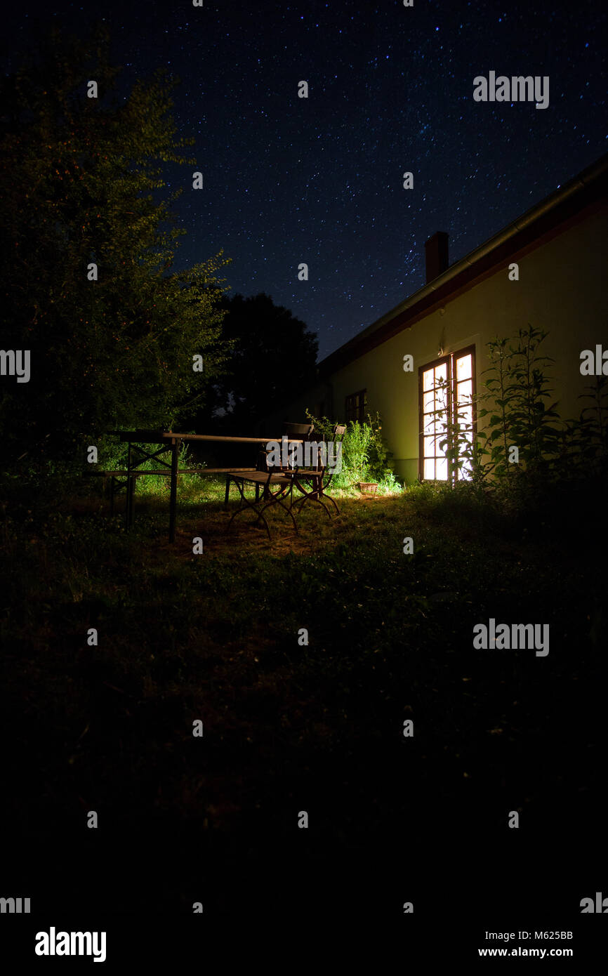 Starry night over an empty table in a garden, scene illuminated by light falling through a window door. Brandenburg, Germnay, Europe. Stock Photo