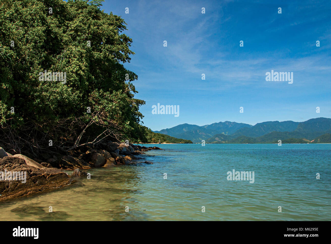 View of rocks, sea and forest on sunny day in Ilha do Pelado, a tropical beach near Paraty, an historic town totally preserved in the Brazilian coast. Stock Photo