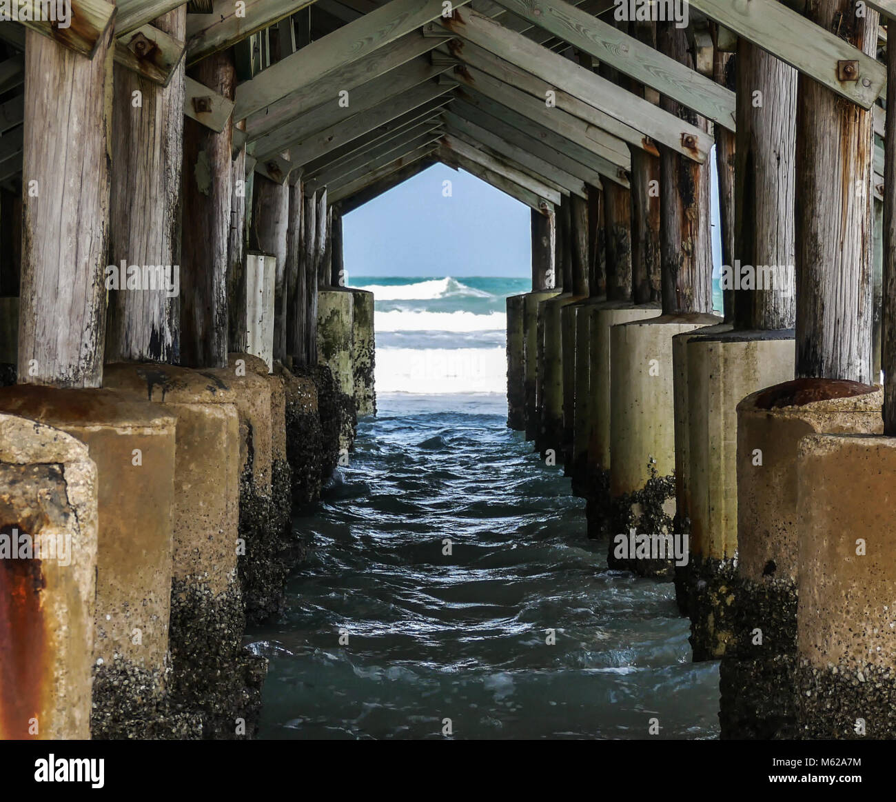 Peering through an archway under a pier seeing waves crashing in the ocean. Stock Photo