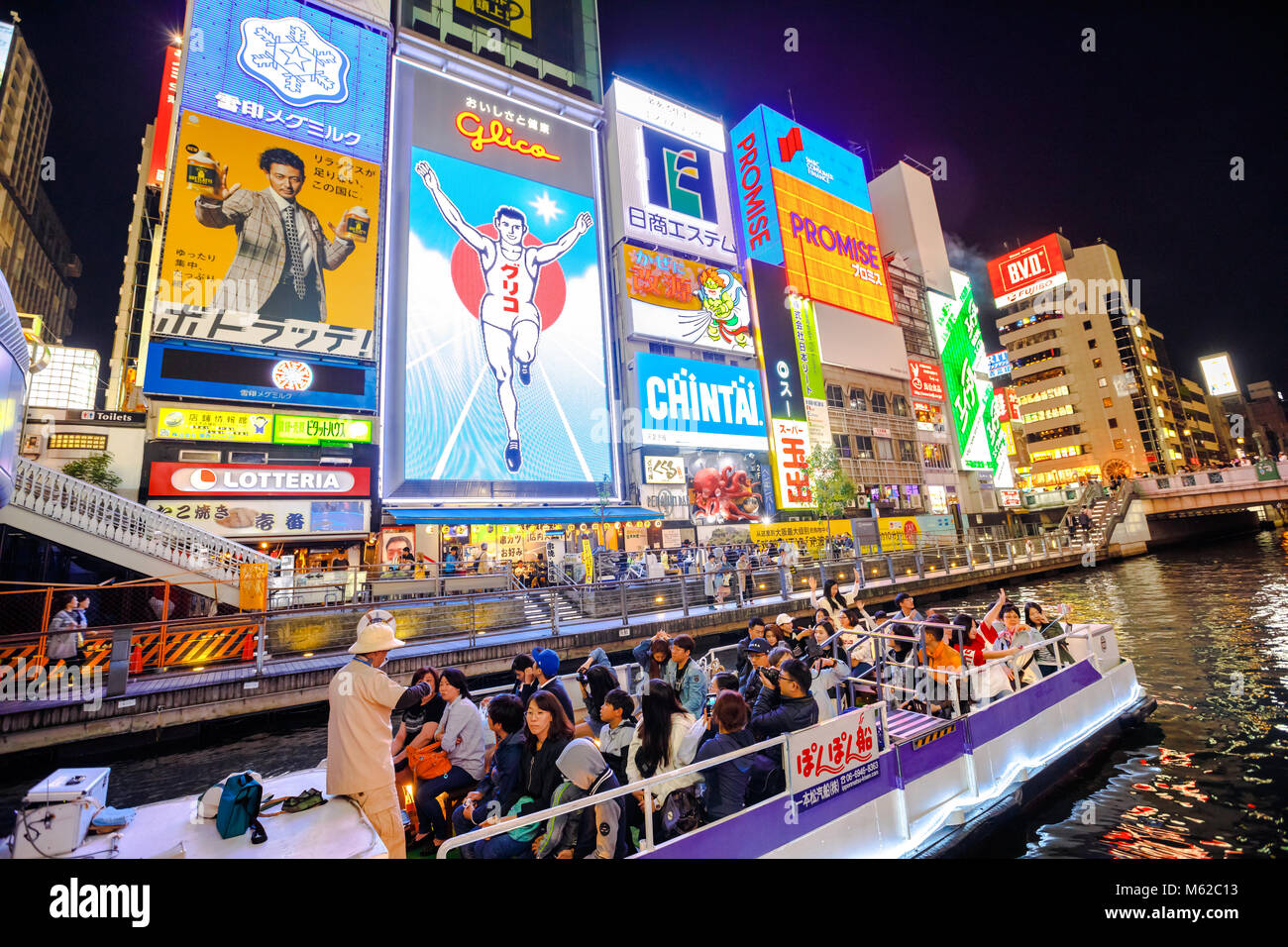 Osaka, Japan - April 29, 2017: touristic boat in the Dotonbori Canal with neon lights of the Glico Running Man sign in Dotonbori street, Namba, a popular shopping and entertainment district. Stock Photo