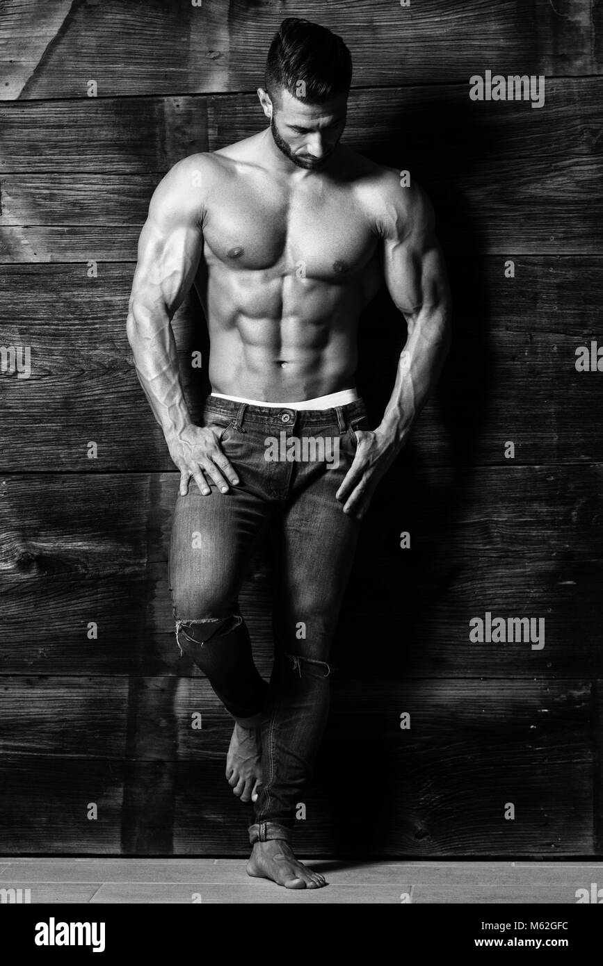 Healthy Young Man Standing Strong Against a Wooden Wall and Flexing Muscles  While Wearing Blue Jeans - Muscular Athletic Bodybuilder Fitness Model Pos  Stock Photo - Alamy