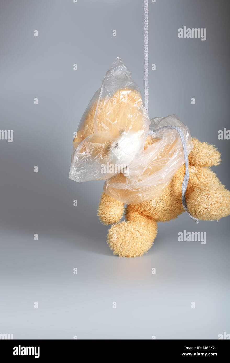 Head of a plush teddy bear is covered by plastic bag. Gray background. Stock Photo