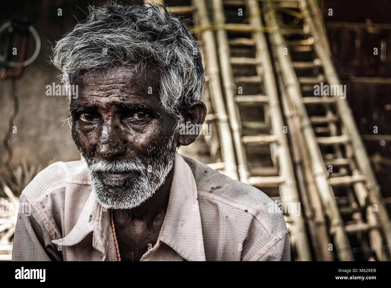 Portrait of Indian elder man with traditional bindi as a third eye, white beard and bamboo ladders on the background in Mysore, Karnataka, India Stock Photo