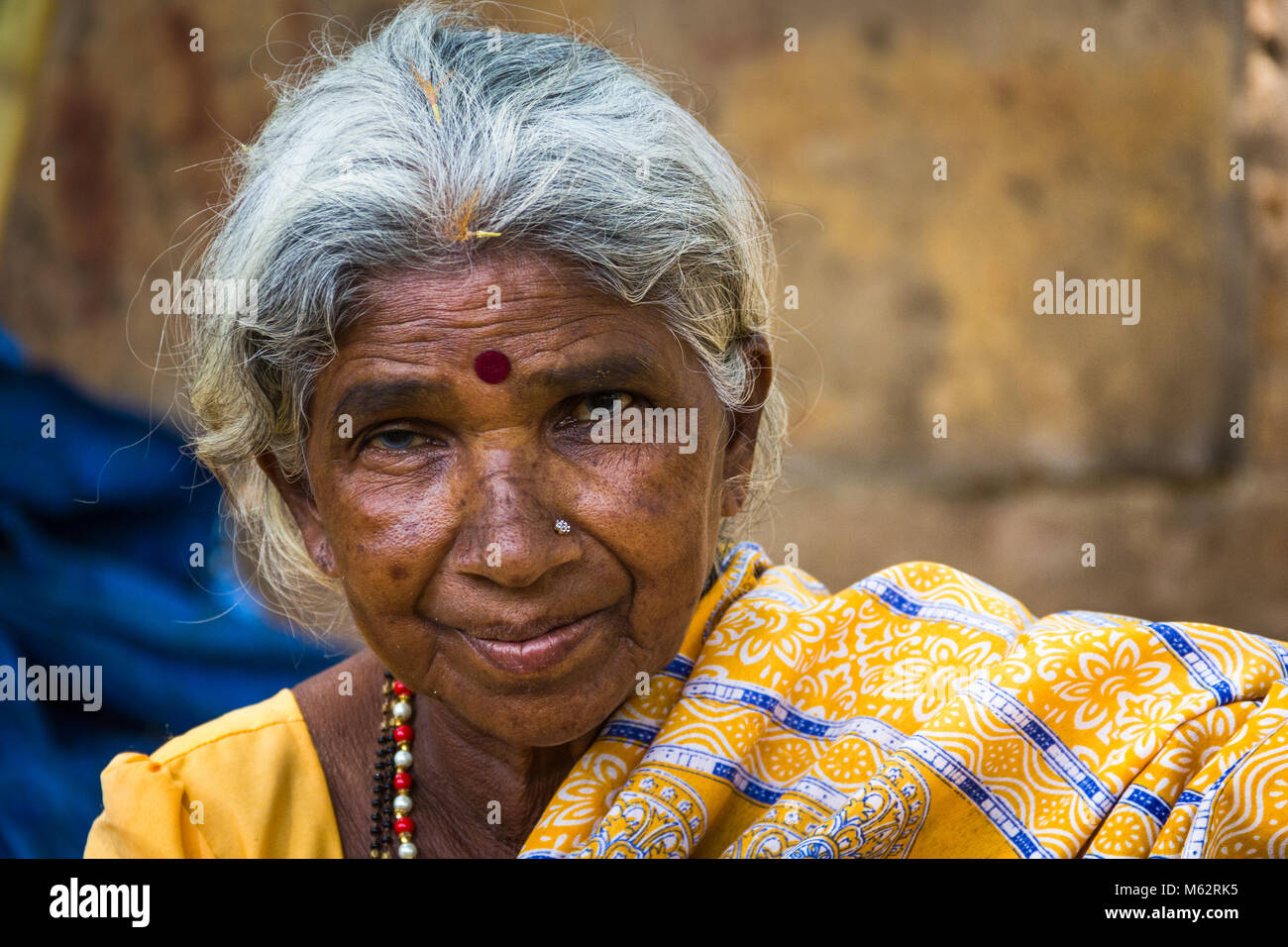 Portrait of Indian elder lady with traditional bindi as a third eye, piercing on nose and wearing a yellow saree in Mysore, Karnataka, India Stock Photo