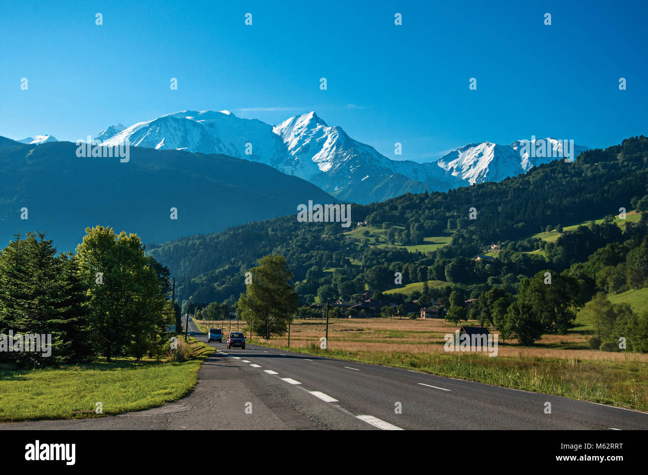 Road among fields, green forest and alpine landscape near Saint-Gervais-Les-Bains. A famous ski resort located near the Mont Blanc in the French Alps. Stock Photo