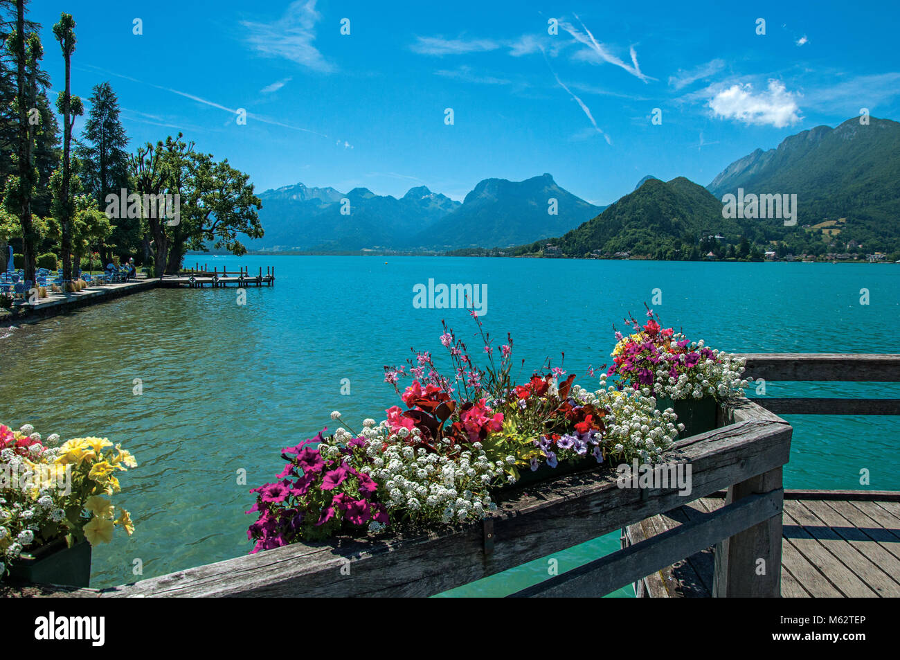Pier with flowers on the Annecy Lake with blue sky mountains landscape ...