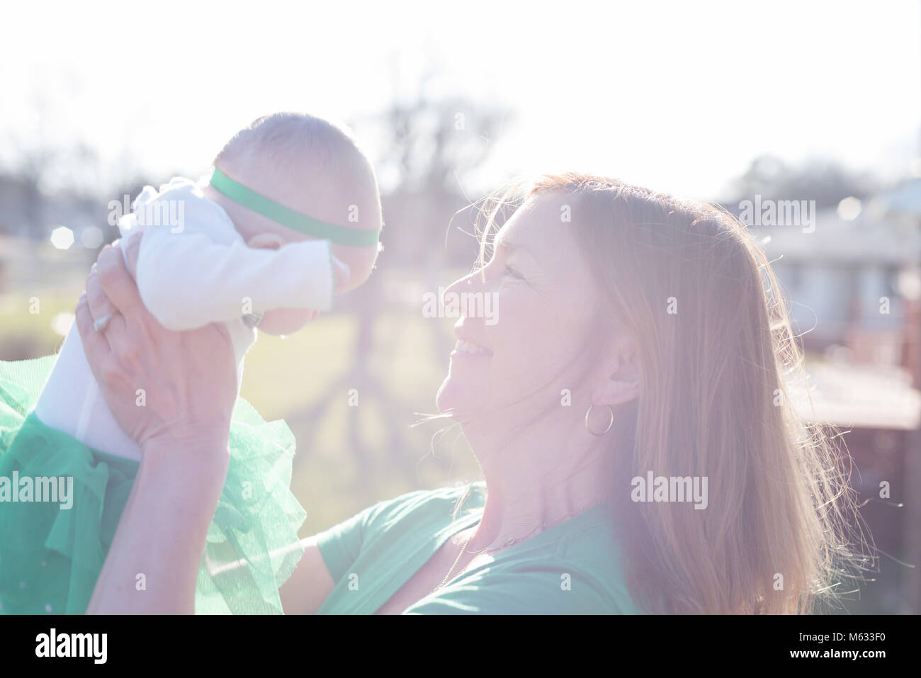 woman holding baby up outside in bright sunlight - overexposed for effect Stock Photo