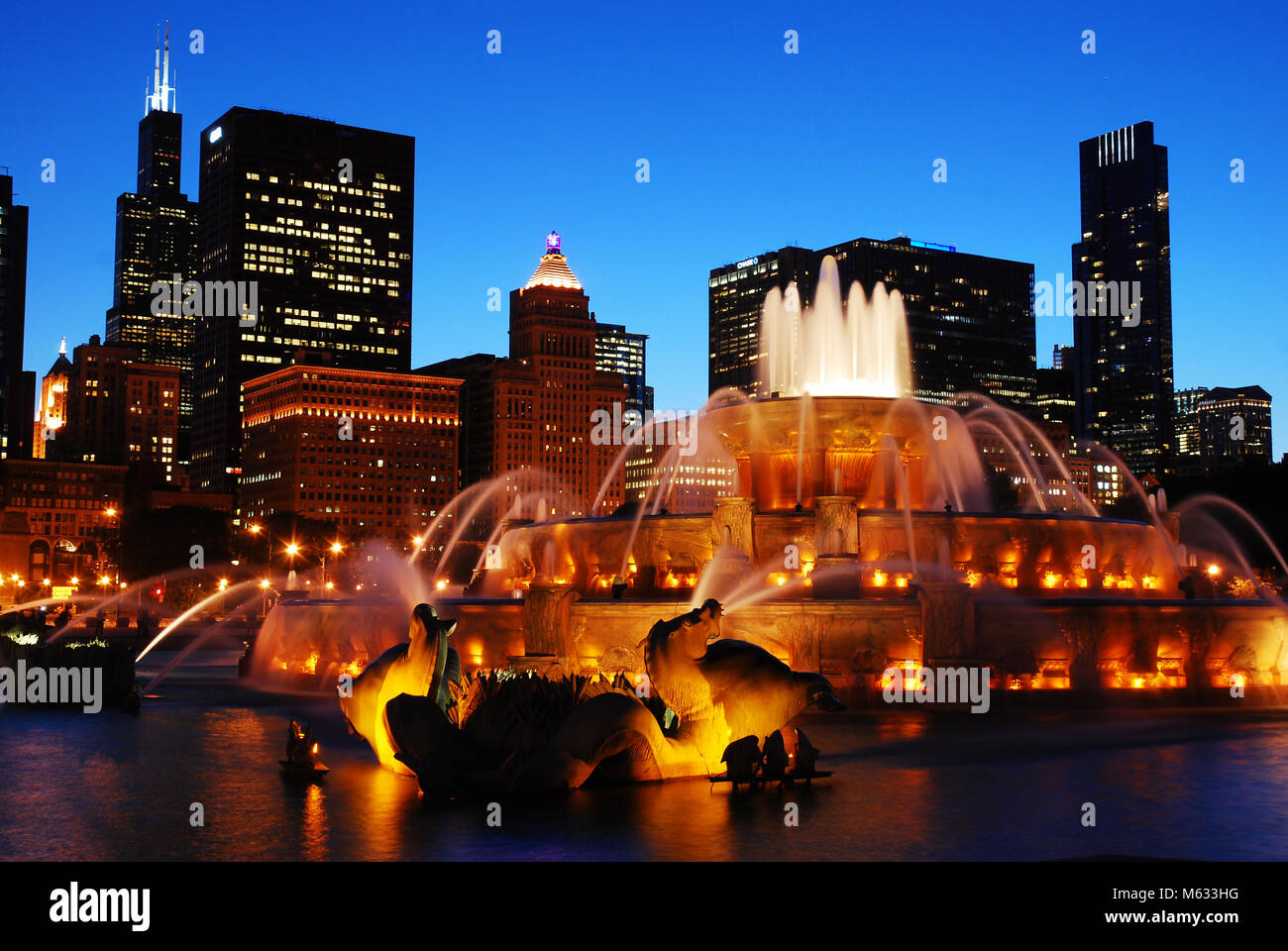 The Buckingham Fountain is illuminated at night, with the lights of the Chicago skyline sparkling behind it Stock Photo