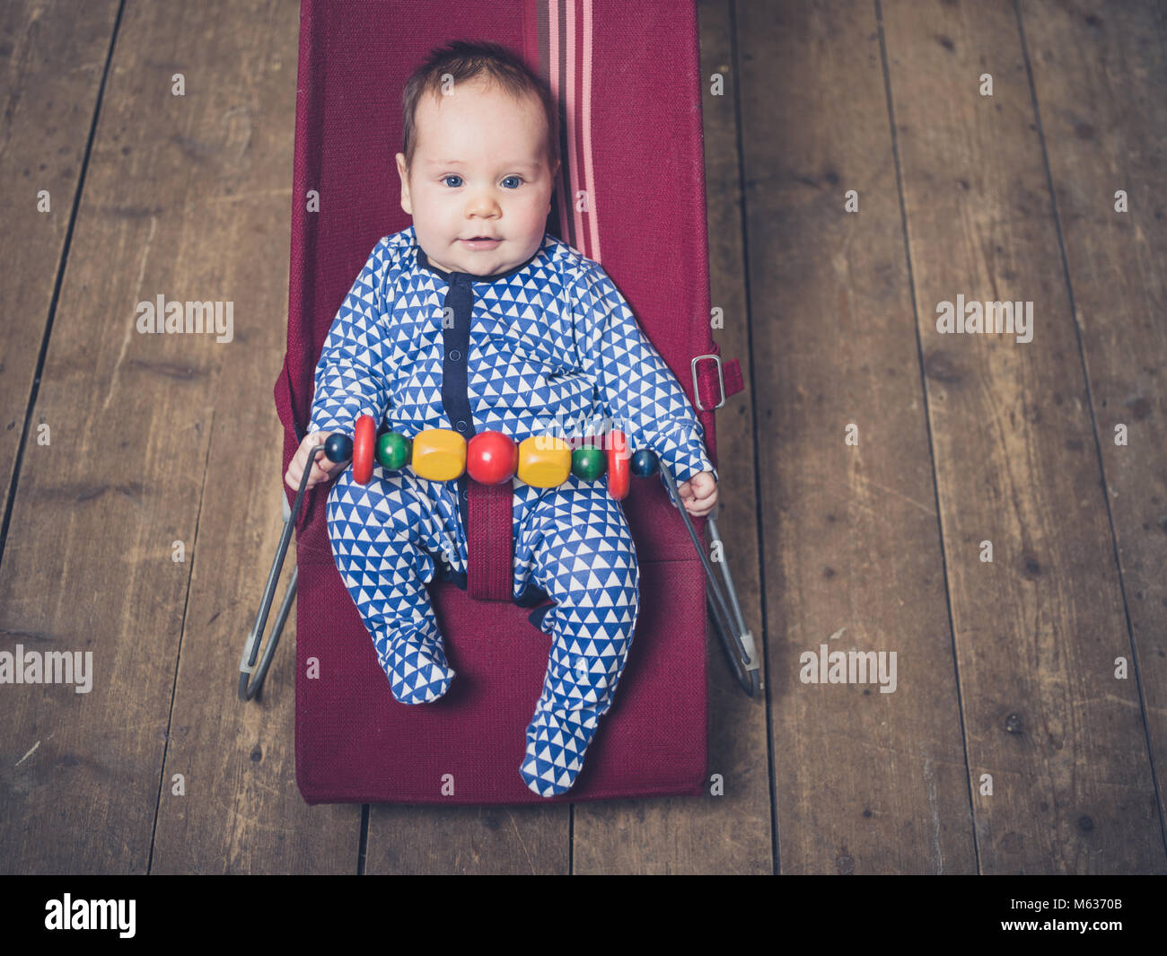 A baby is sitting in a vintage bouncy chair on the wooden floor Stock