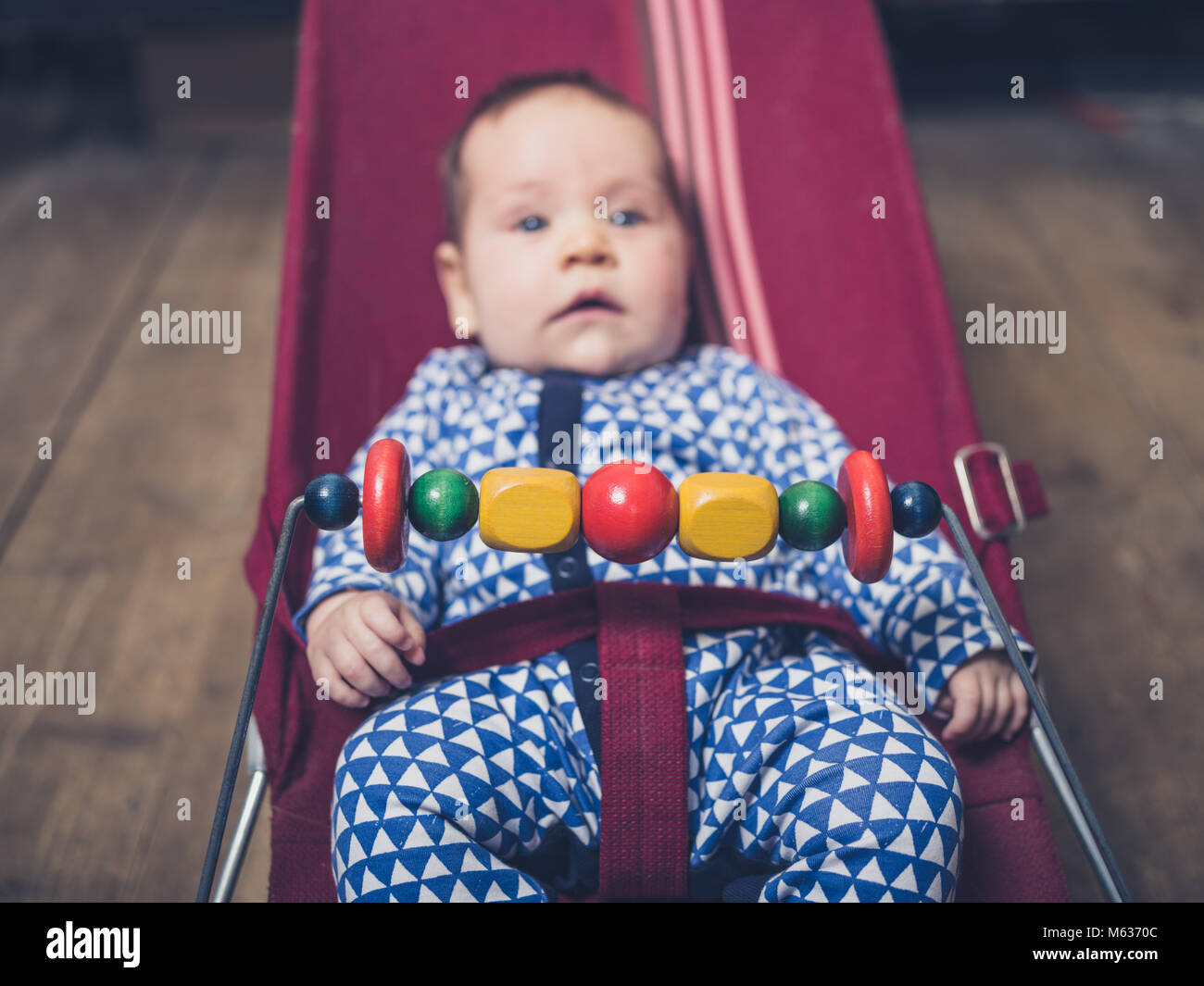 A baby is sitting in a vintage bouncy chair on the wooden floor Stock Photo