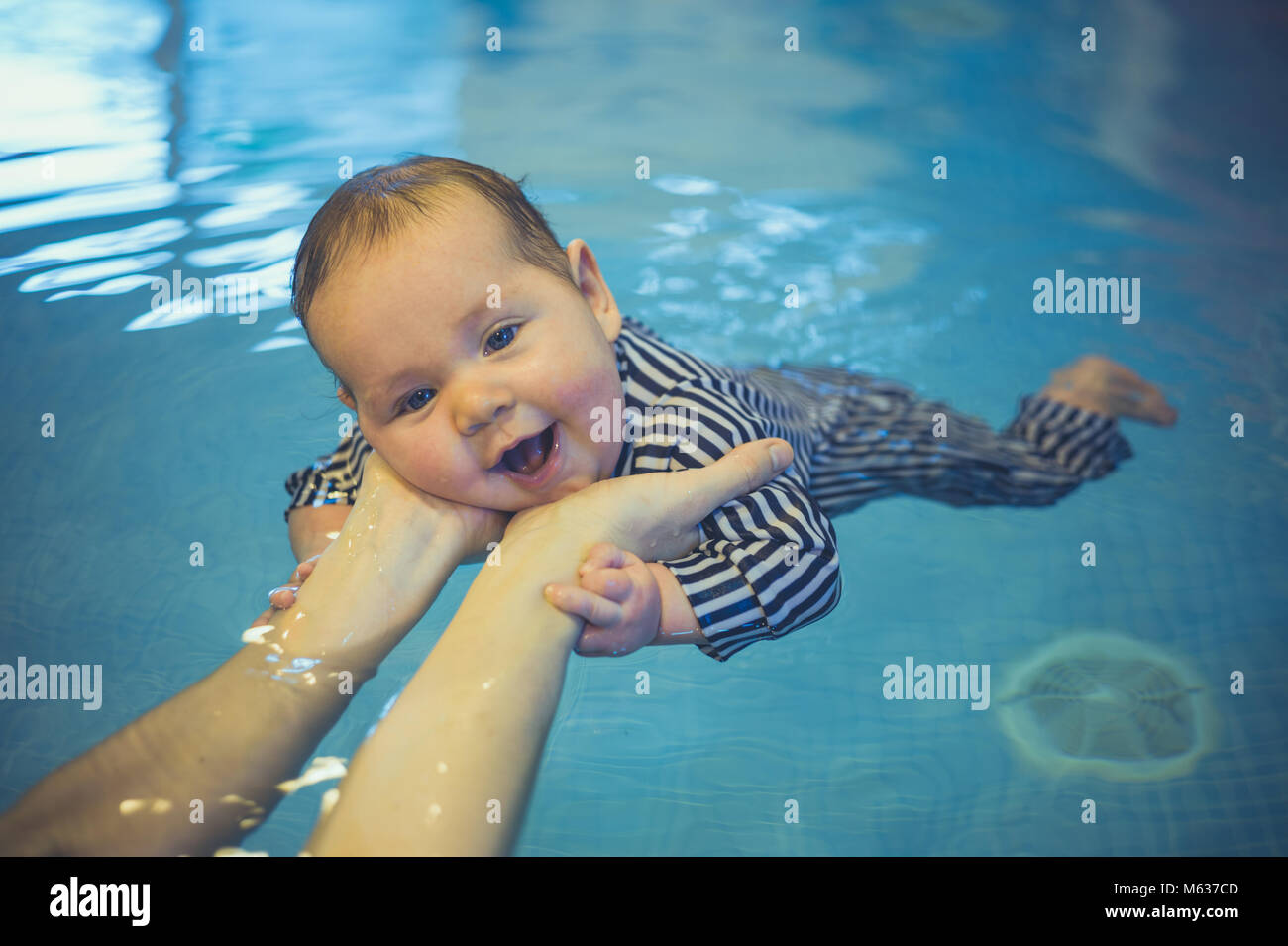 A little baby is swimming in a pool with help from his mothers hands