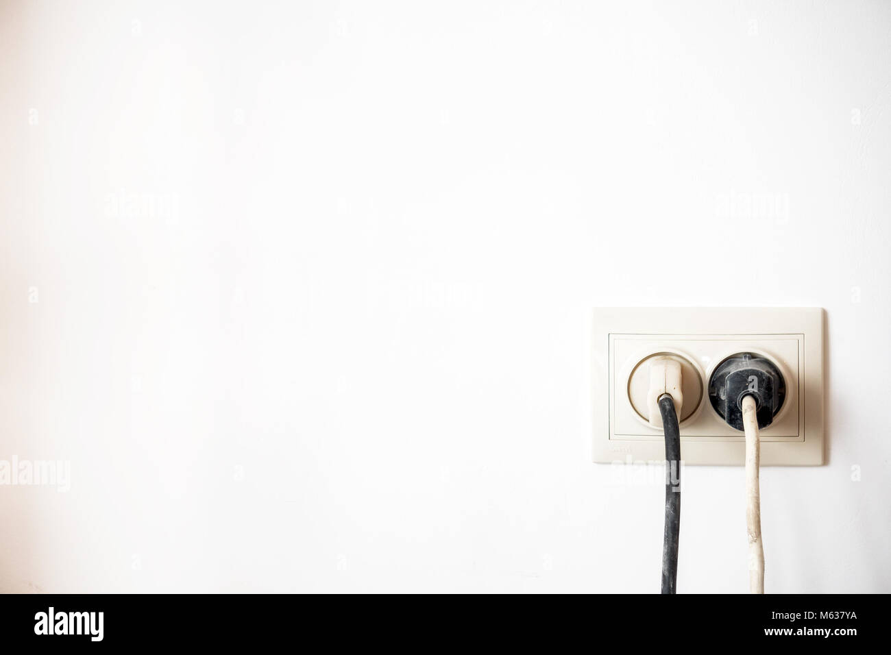 Electric socket with two stuck electric plugs on a white wall. Power