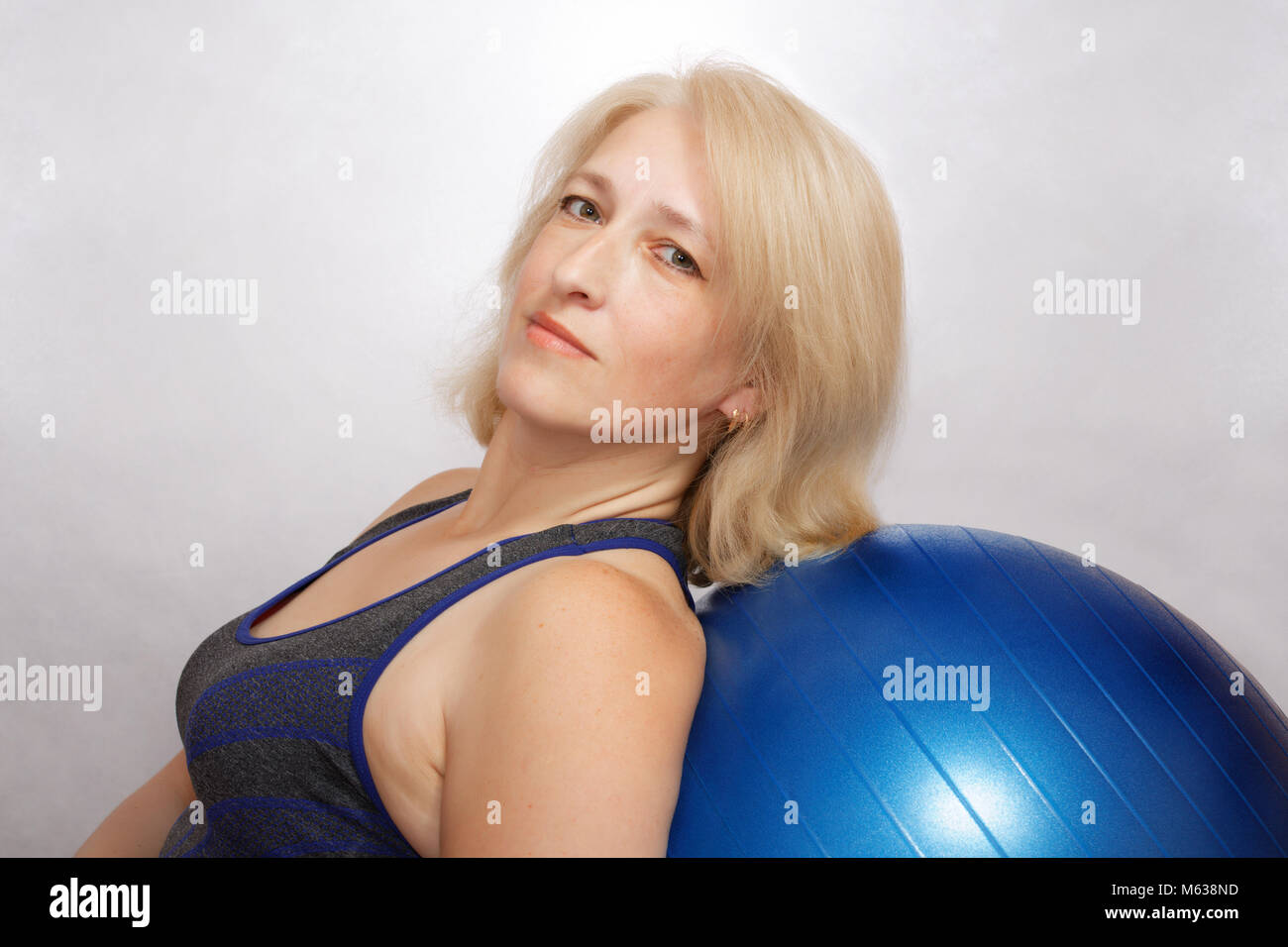 A middle-aged woman performs an exercise in Pilates, is leaned on fitball. Affordable sports at home Stock Photo