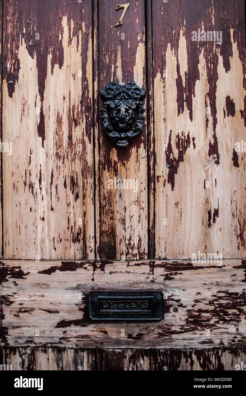 Close up of wooden door in England with paint peeling and ornate iron door knocker Stock Photo