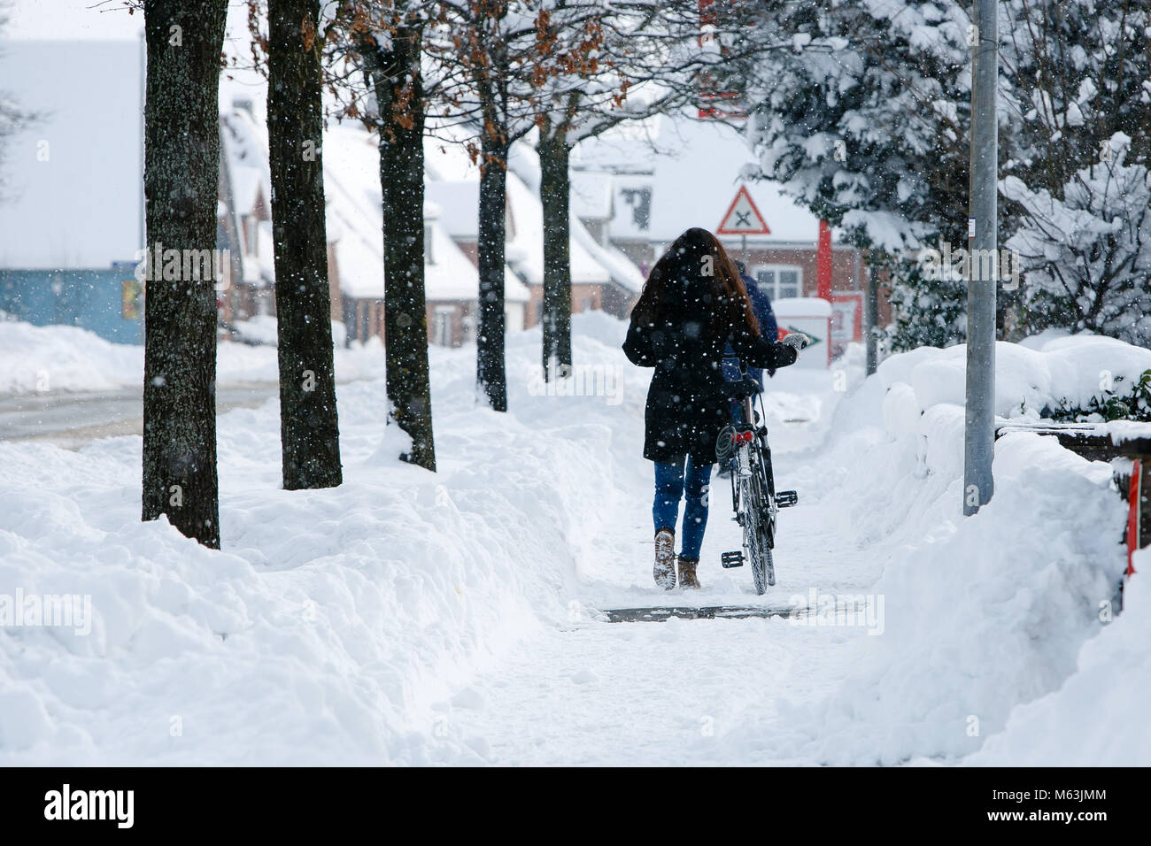 Bredstedt, Germany. 28th Feb, 2018. A cyclist pushing her bicycle through the fresh snow in Bredstedt, Germany, 28 February 2018. Strong snowfall lead to a difficult traffic situation on the streets of Nordfriesland. Credit: Frank Molter/dpa/Alamy Live News Stock Photo