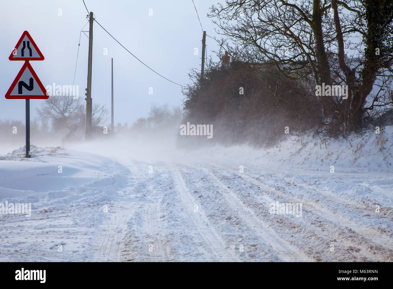 UK Weather: Norfolk, UK. 28th February, 2018. Heavy snow and blizzard conditions hit Norfolk. With temperatures reaching as low as -5c and a windchill of -14c. Snow is seen here drifting across a road making it almost unpassable.  This cold weather has been named Beast From the east. Stock Photo
