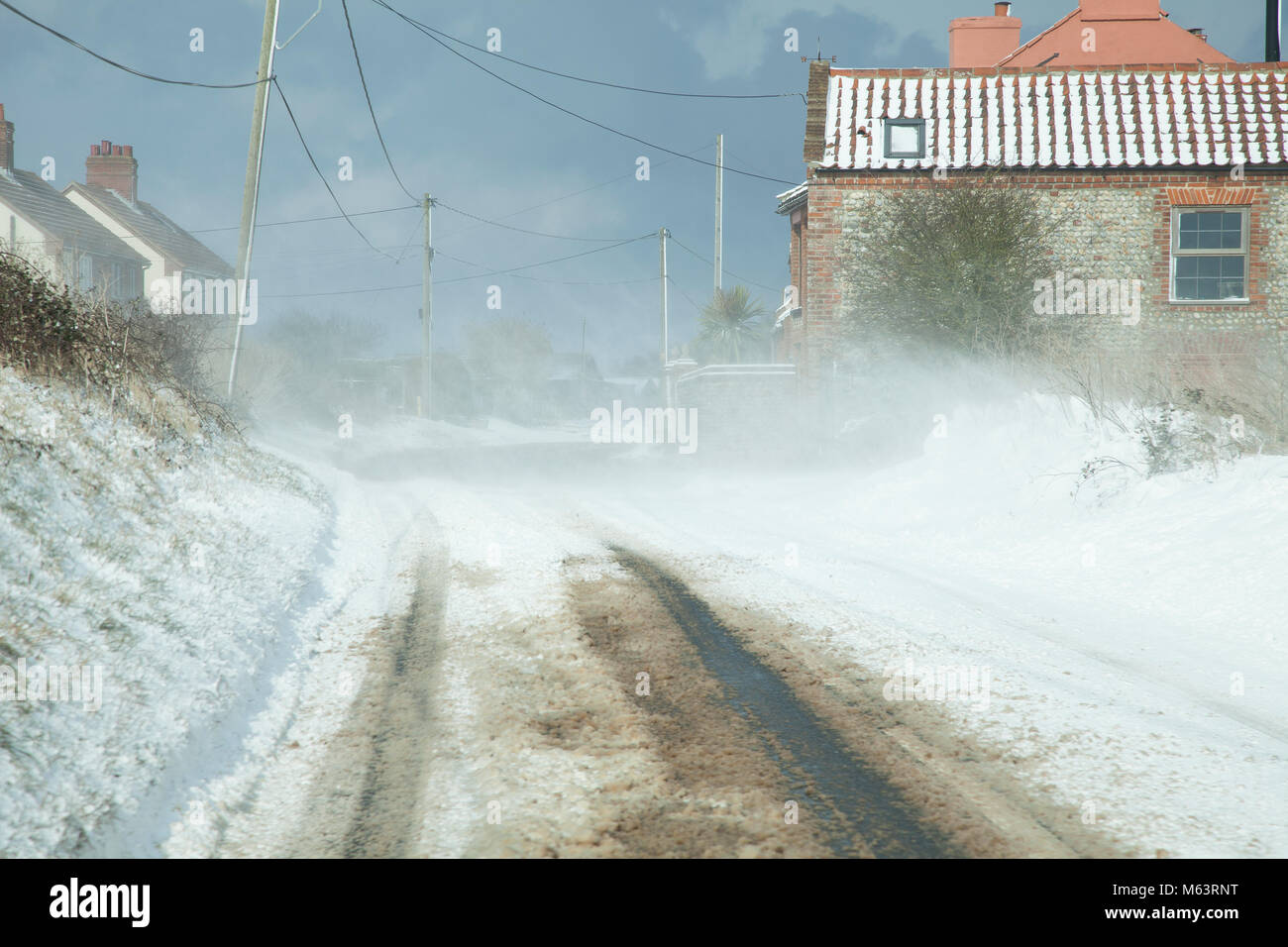 UK Weather: Norfolk, UK. 28th February, 2018. Heavy snow and blizzard conditions hit Norfolk. With temperatures reaching as low as -5c and a windchill of -14c. Snow is seen here drifting across a road making it almost unpassable.  This cold weather has been named Beast From the east. Stock Photo
