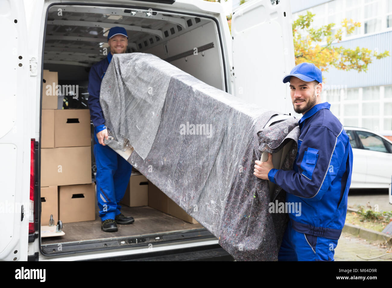 Two Young Delivery Men In Uniform Unloading Furniture From Vehicle Stock Photo